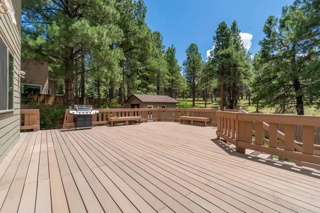 Spacious wooden deck overlooking pine trees and a small cabin under a clear blue sky